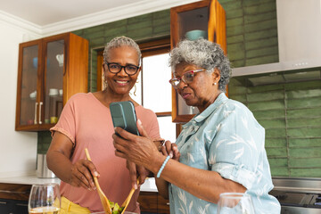 Fototapeta premium Senior African American woman and senior biracial woman share a moment in a kitchen