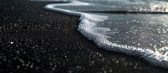 A close-up view of a wave crashing onto a beach with black sand. The water creates intricate patterns as it meets the shore, showcasing the power and beauty of nature. - Powered by Adobe