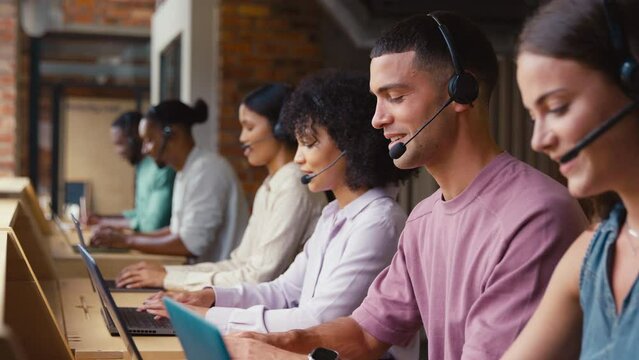 Multi-Cultural customer support or telesales team in modern open plan office wearing headsets and talking with customers - shot in slow motion