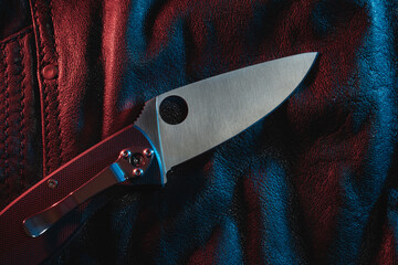Close-up photo of a pocket knife on a leather jacket. - obrazy, fototapety, plakaty
