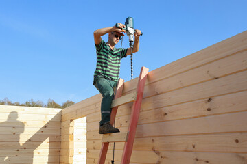 Builder drilling top log to join wall timber, building new rural timber house