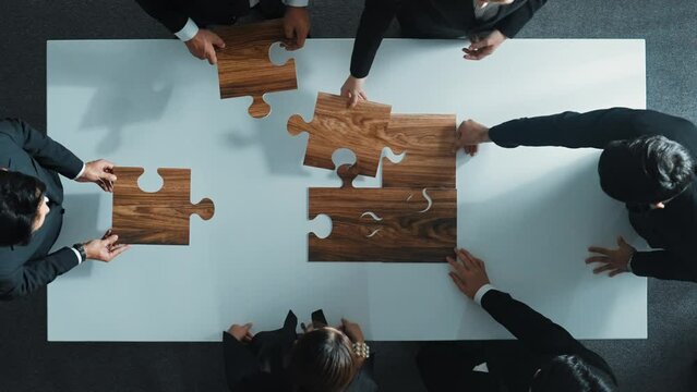 Top view of business people putting jigsaw together at meeting room. Professional marketing team standing at table while gathering puzzle piece. Show unity, cooperation and team working. Directorate.
