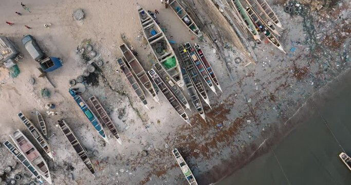 Aerial 360 zoom out.   Colourful pirogue boats lie anchored in the polluted Senegal River. Plastic pollution lines the ocean front, Saint-Louis, Senegal, Unesco World Heritage Site
