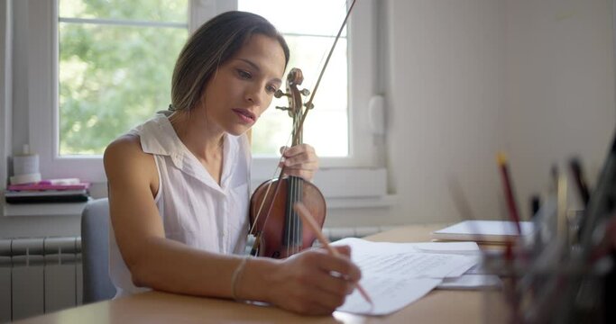 Female violinist practicing playing violin by reading sheet music at home