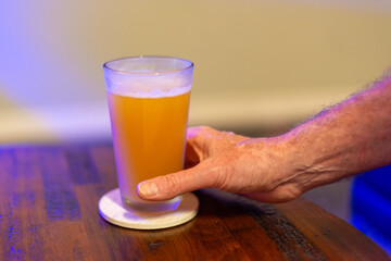 A male holds the bottom of a tall cold glass of beer. There's froth at the top of the glass and...