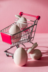 Porcelain Easter eggs,bunny and shopping cart on a pink background.