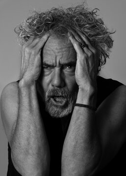 Frustrated man with wild hair, holding his head. Black and white photograph.