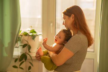 Caucasian woman tenderly holds her newborn son while standing near the window. 