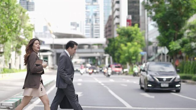 4K Confidence Asian businessman and businesswoman office worker holding briefcase and laptop computer walking street crosswalk in the city. Business people company employee go to work in the morning.