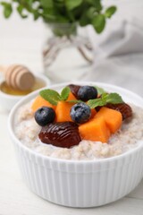 Delicious barley porridge with blueberries, pumpkin, dates and mint in bowl on white table, closeup