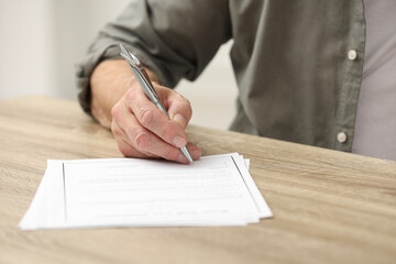 Senior man signing Last Will and Testament at wooden table indoors, closeup