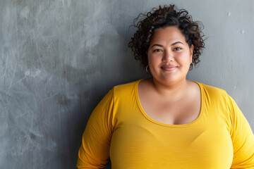 Confident Curvy Woman in Yellow Shirt Smiling Against Grey Textured Background, Expressing Positivity and Self-love - obrazy, fototapety, plakaty