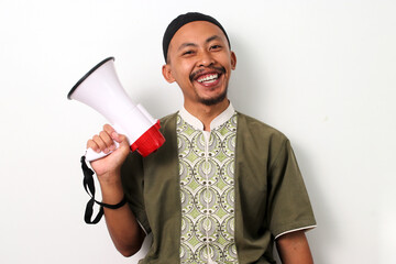 Confident Indonesian Muslim man in koko shirt and peci holds a megaphone, ready to speak. Isolated...