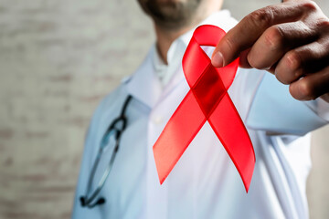 Out of focus doctor holding a red ribbon as a sign of awareness. - Powered by Adobe