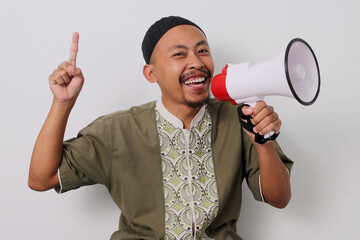 Indonesian Muslim man in koko and peci holds a megaphone and points to the side, directing...