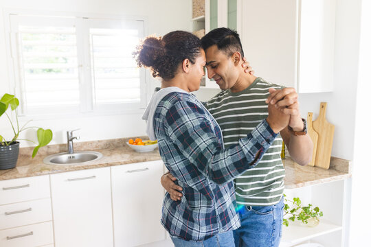 Gay biracial couple shares a tender moment, dancing in a bright kitchen