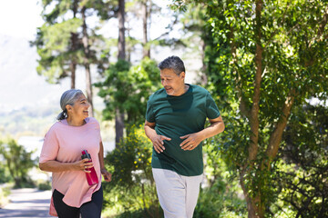 Senior biracial couple jogging together in a lush park