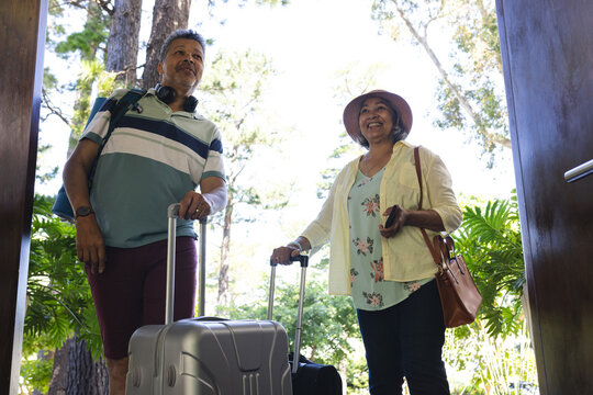 Senior biracial couple in casual travel attire ready for a trip, with luggage in hand