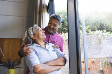 Senior biracial couple shares a tender moment, the man embracing the woman from behind