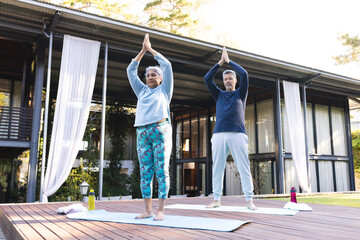 Senior biracial woman and biracial man practice yoga outdoors at home