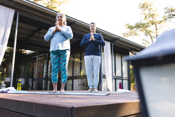 Senior biracial woman and biracial man practice yoga outdoors, at home