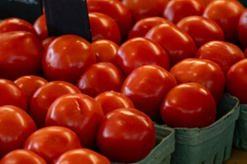 A harvest of large fresh organic tomatoes stockpiled in a crop bunch for sale at a farmers' market. The raw tomatoes are stacked exposing the dark red color of the vegetables with smooth shiny skin.