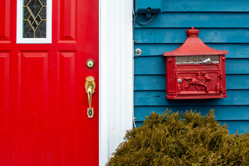 A bright retro red metal mailbox, or letterbox, is affixed to the exterior wall of a blue wooden...