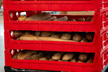 Multiple red plastic trays filled with fresh French bread, buns, and baguettes. The bakery storage...
