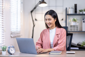 Portrait of happy young asian woman accountant working documents on laptop and  phone desk using calculator for calculate finance report in home office