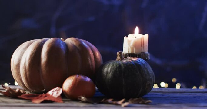 A candle burns beside pumpkins, evoking autumn vibes