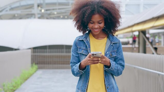 Black young woman using smart phone and smile with walking in the city outdoor. Happy african student, young female walking with mobile by a building