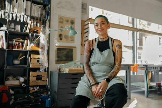 Smiling female designer sitting on background of own workshop and looks camera