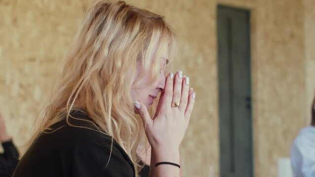 Blonde woman meditating sitting in lotus pose with hands in namaste in gym. Female with closed eyes doing spiritual mental yoga practice in group. Inner life, harmony balance in conscience concept.