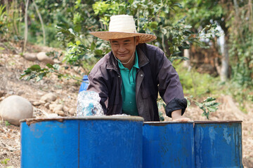 Asian man farmer is working, preparing water into blue buckets in garden. Concept, Solve problems lacking of water in agriculture by prepare water for watering plants in drought season.   