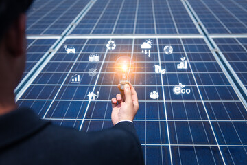 Businessman's hand holds a light bulb on a solar panel future energy investment innovation,...