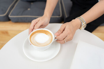 Closeup of the hands of a business woman Hold an espresso coffee cup with milk foam inside. On the...