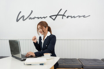 Female executive is an Asian stock investor wearing a suit Analyze company business graphs and profits with a laptop, have industry books. Drink coffee and relax in the office's white cafe.