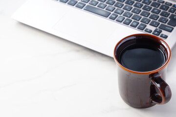 コーヒーを飲みながらノートパソコンでデスクワーク中のイメージ	
