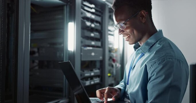 Happy man, engineer and laptop in server room for database update, cyber security or code. Computer, smile and African technician in data center for information technology, typing and programming