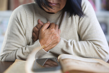 Senior adult elderly woman asian sits in a chair hand holding her chest with disease chest pain...