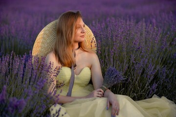Woman poses in lavender field at sunset. Happy woman in yellow dress holds lavender bouquet....