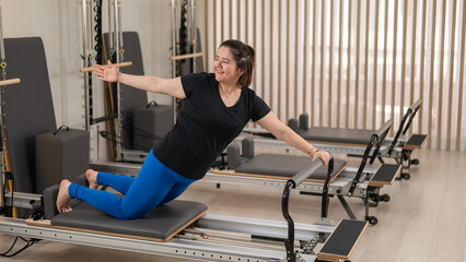 Overweight caucasian woman doing pilates exercises on a reformer. 