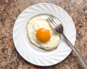 Fried egg on a white plate with a fork on the table