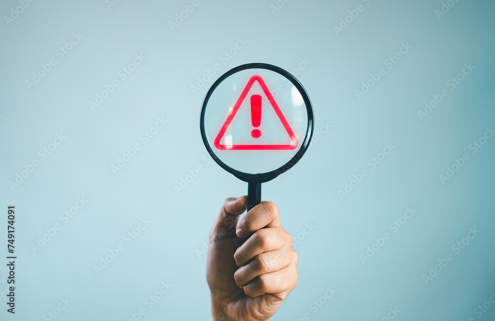 Poster Hand holding magnifying glass with red triangle caution warning sign for notification error and maintenance concept.