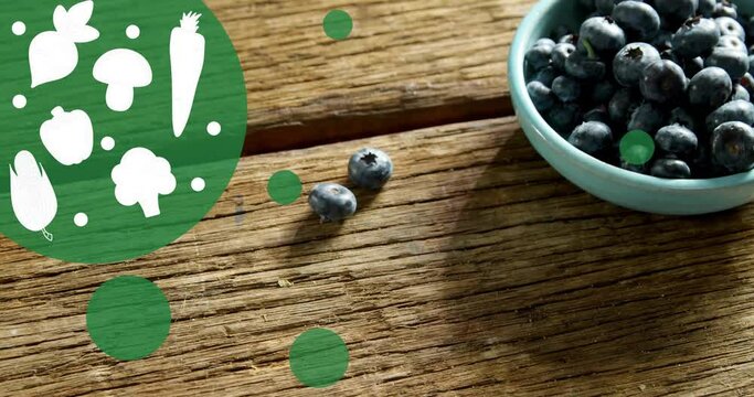 Animation of vegetable icons over blueberries in bowl on table