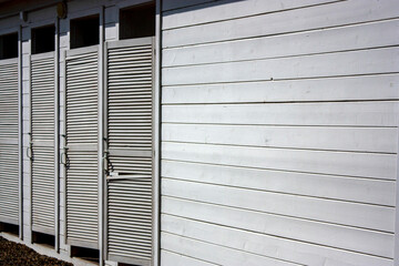 Changing cabins on the beach. Wooden wall made of white boards. Wooden doors painted white.