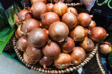 Fresh yellow and red onions fill a basket at a market stall - 749183875