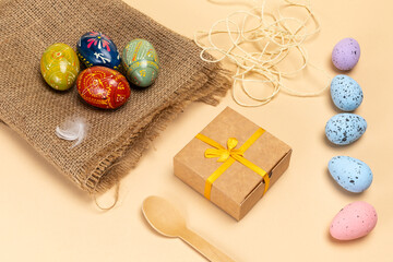 Easter eggs on a sackcloth bag and a gift box on the beige background.