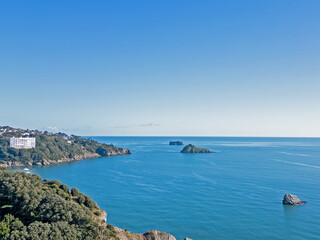 An aerial drone photograph of Meadfoot and Tor Bay in Torquay Devon with a view of the blue sea and blue sky and shag rock, thatcher's rock and ore stone in the distance