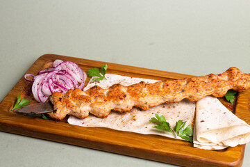 Delicious and juicy chicken shish kebab on a wooden board with onion rings and parsley.